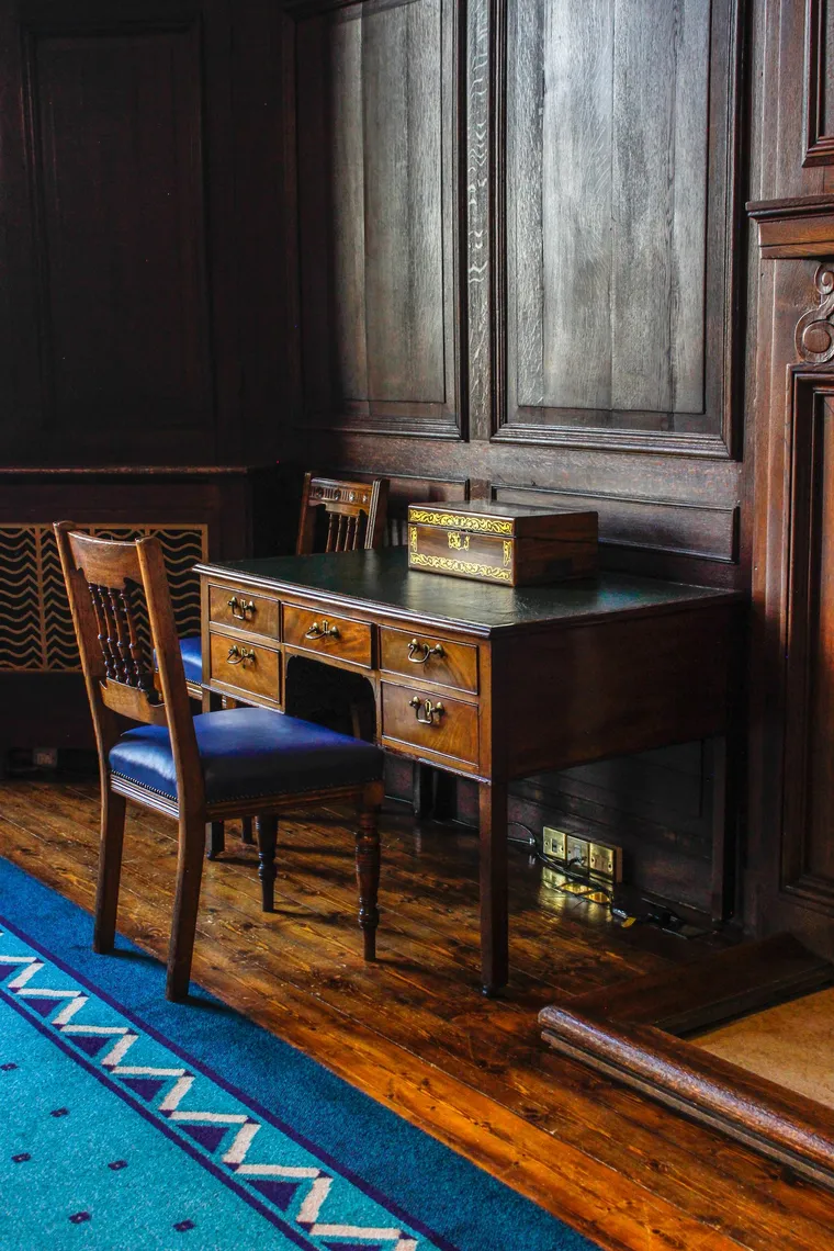 An antique writing desk and chair in a wood-paneled study